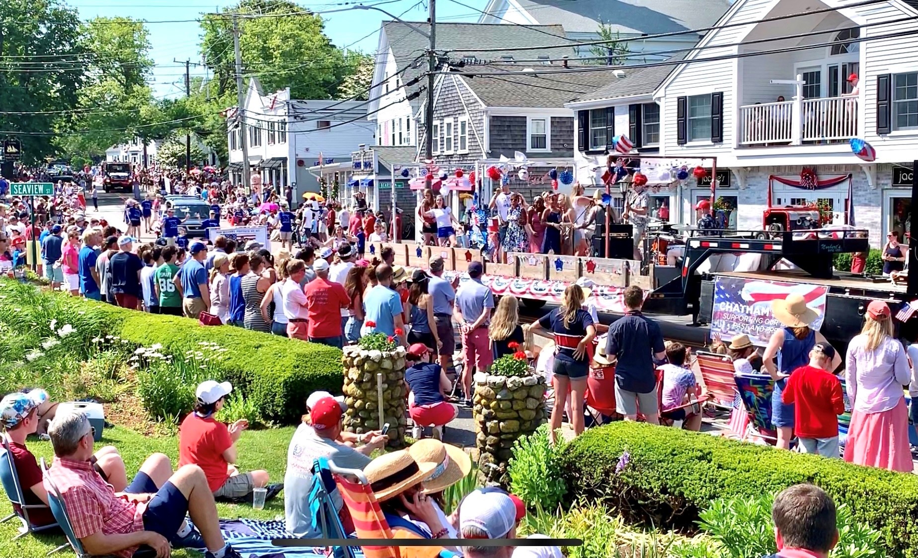 A festive parade with a float, crowd in red, white, and blue, celebrating a national holiday on a sunny day.