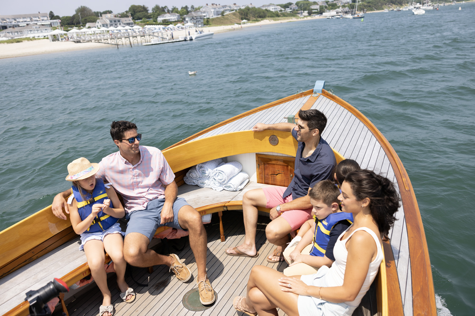 A family relaxes on a boat ride near a beach, enjoying the sunny weather with life vests on some children.