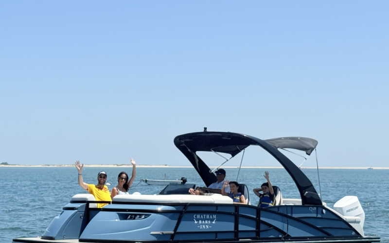 A group of people are enjoying a ride on a pontoon boat named "Chatham Bars Inn" on a sunny day.