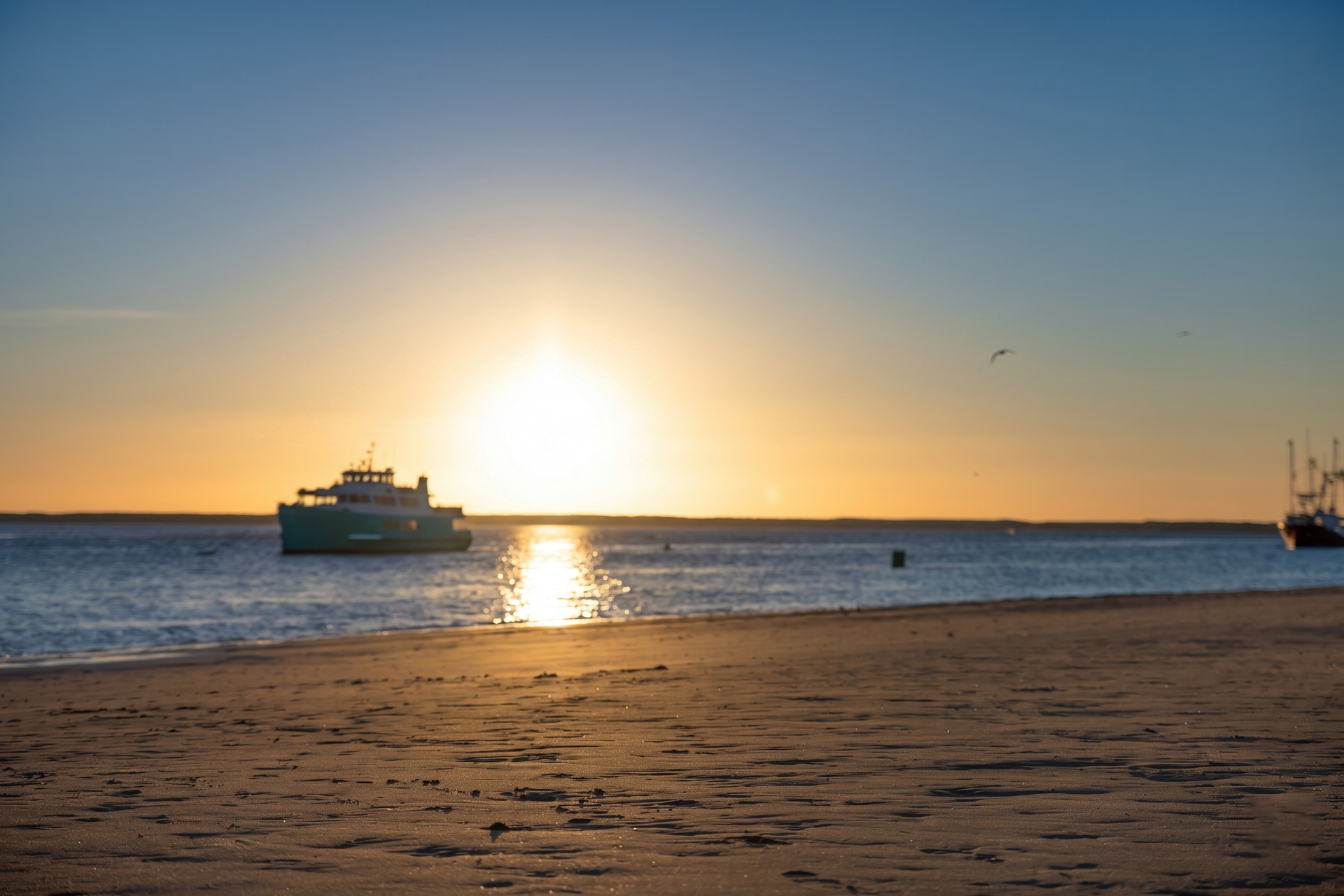A serene beach scene with a boat on the water at sunset, capturing a tranquil moment.