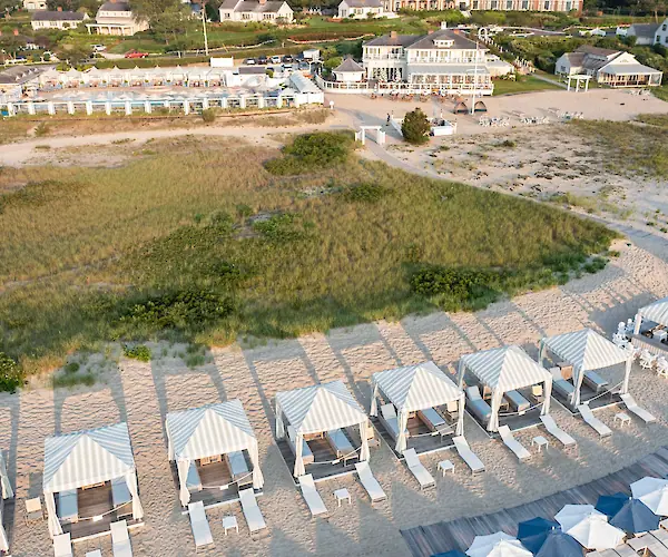 Aerial view of a beachside resort with cabanas, deck chairs, grassy areas, and adjacent buildings.