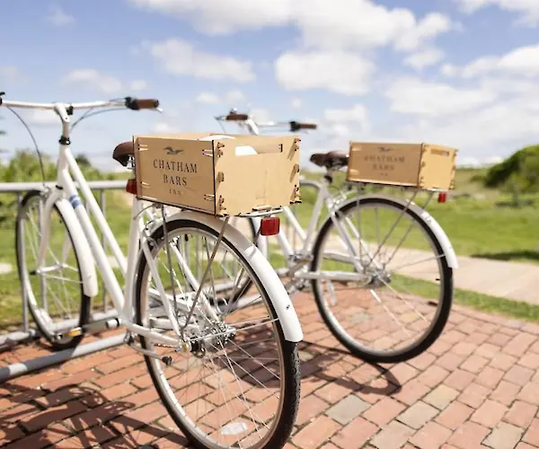 Two white bicycles with "Chatham Bars Inn" boxes are parked on a brick path, with a person walking in the background.