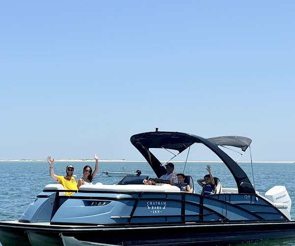 A group of people is waving from a blue pontoon boat on the water, under a clear blue sky.