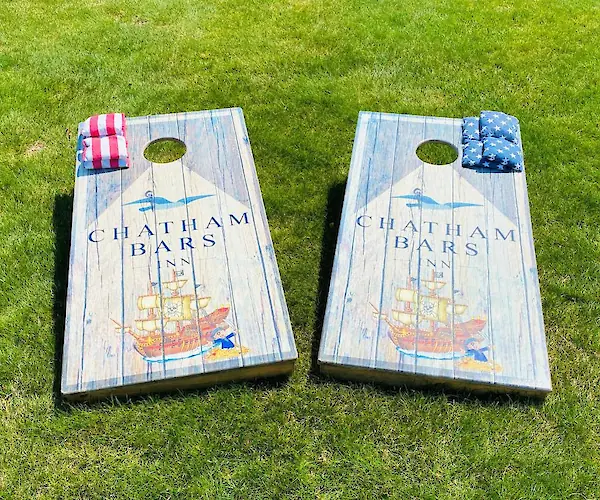 Two cornhole boards with a ship design and "Chatham Bars Inn" text on grass, featuring red and blue bean bags.