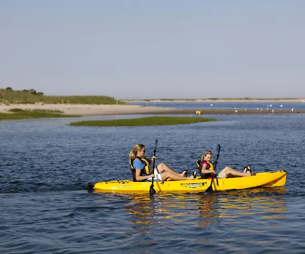 Two people are kayaking a yellow kayak on a calm body of water, surrounded by grassy banks and blue sky.