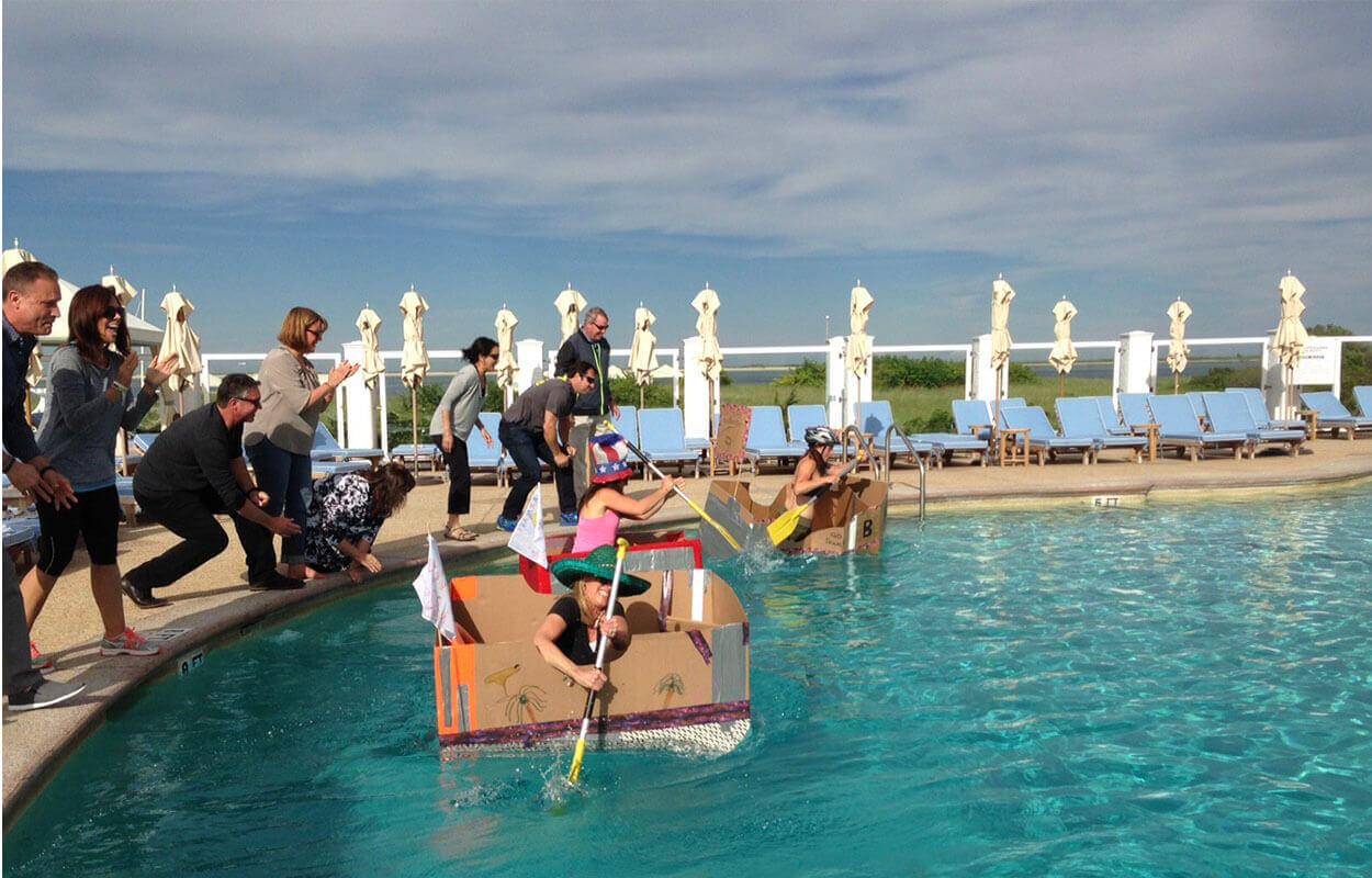 Colleagues racing cardboard boats in the pool