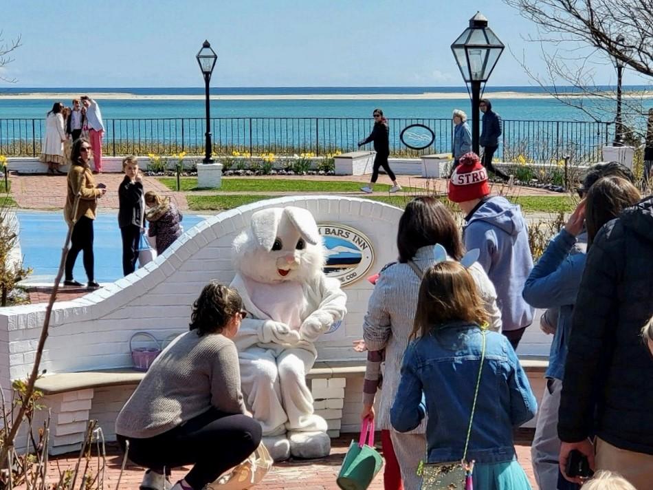 People gathered around a person in a bunny costume near a lakeside park.