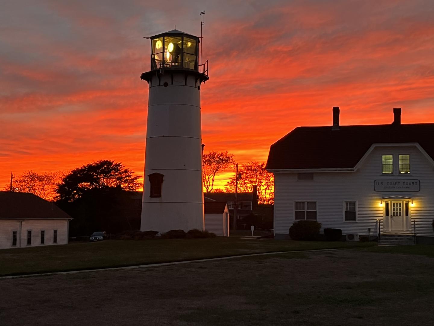 Lighthouse and building silhouetted against a vibrant orange sunset.