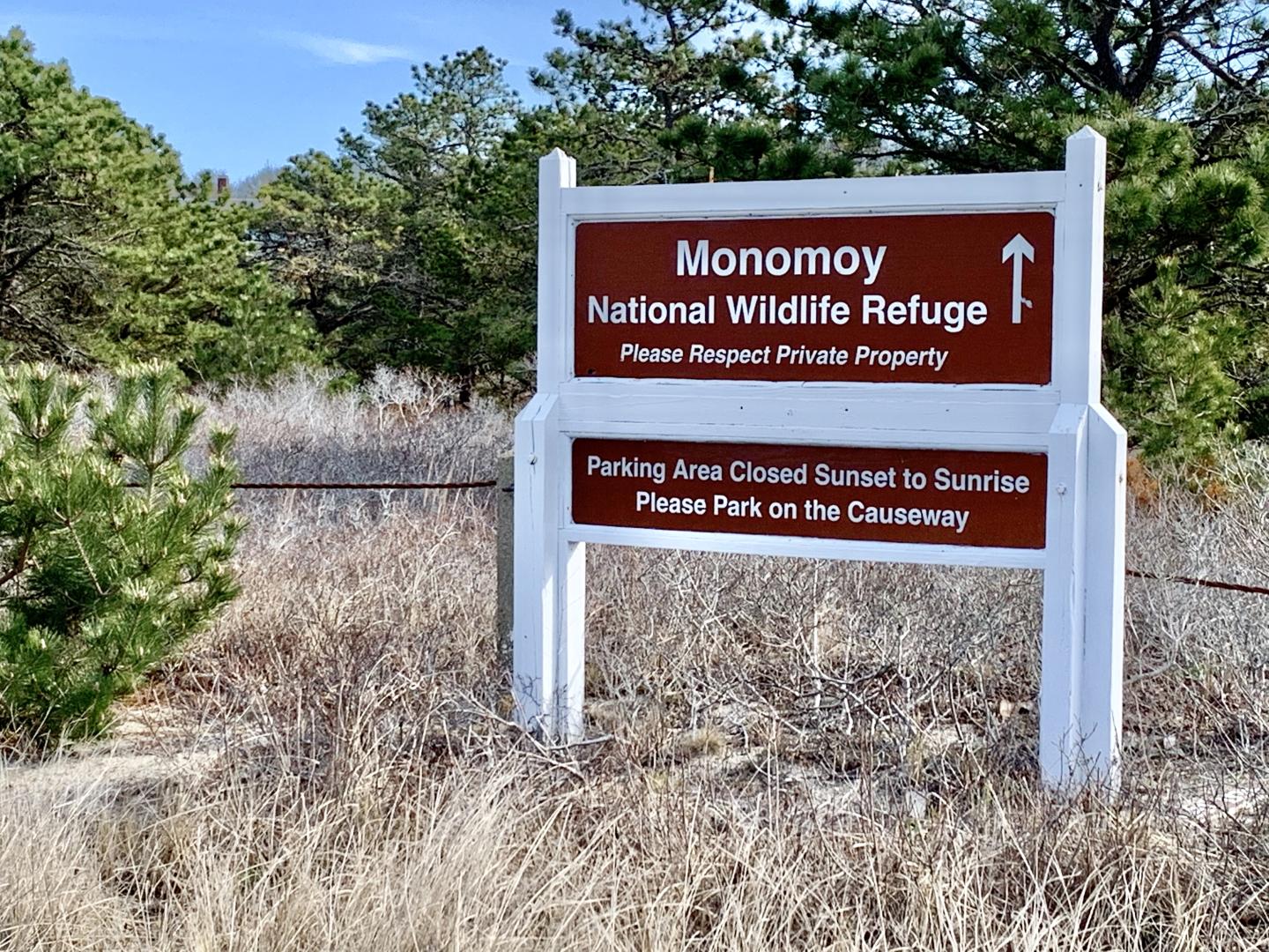Sign for Monomoy National Wildlife Refuge surrounded by trees and grass.