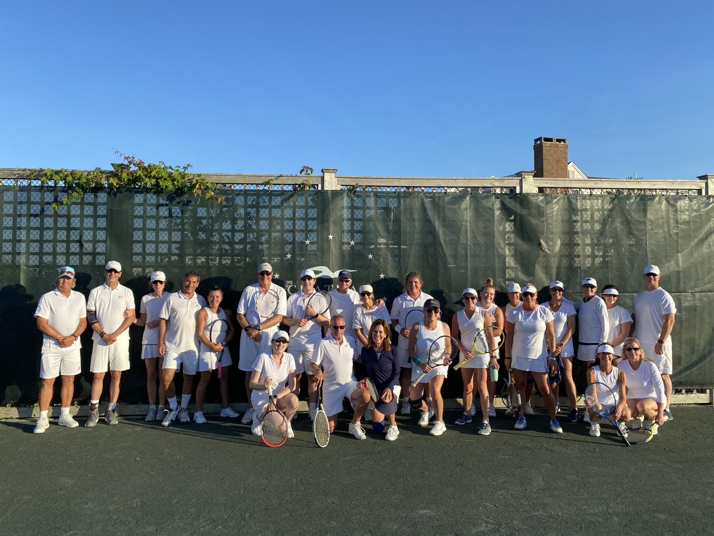 Group of people in white tennis outfits posing outdoors.