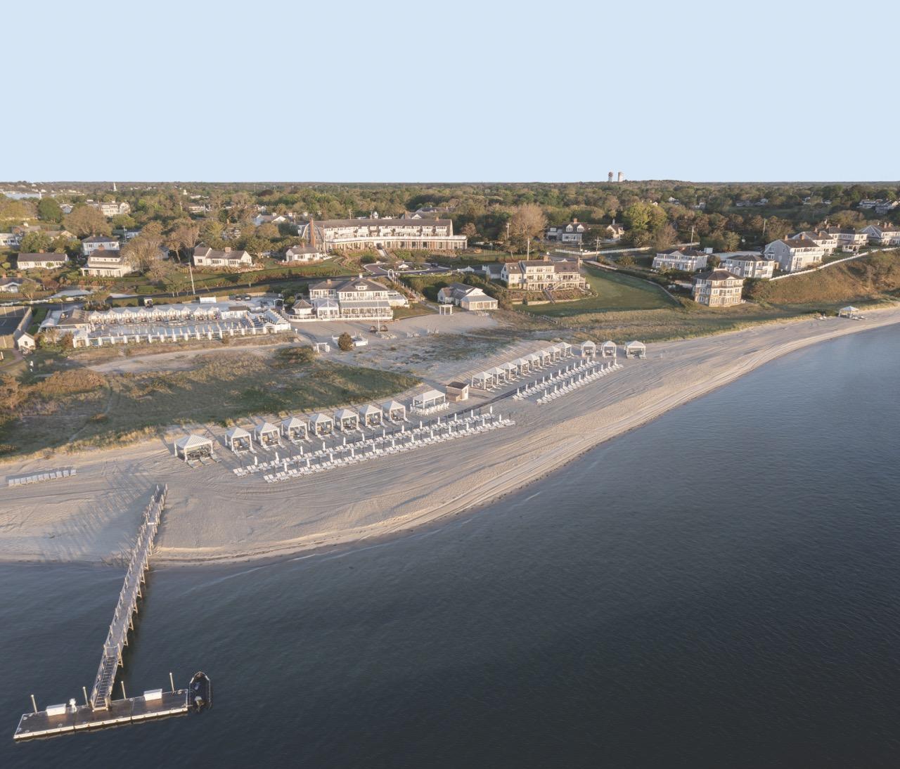 Aerial view of a beach with sunshades, pier, and nearby buildings.