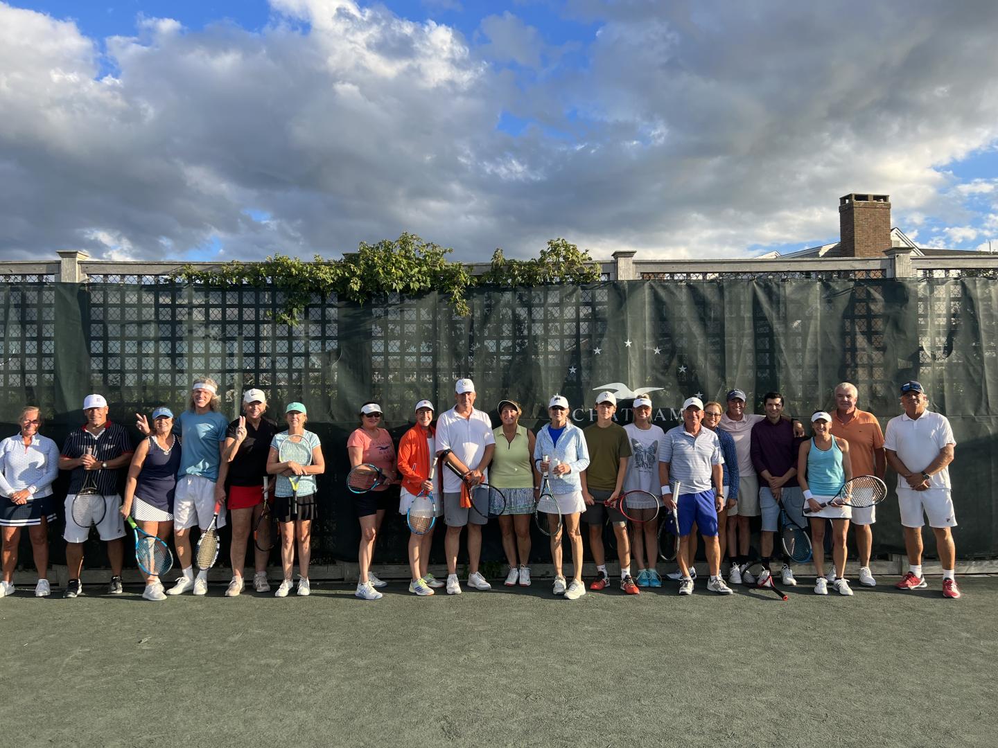 Tennis players lined up on a court under a cloudy sky.