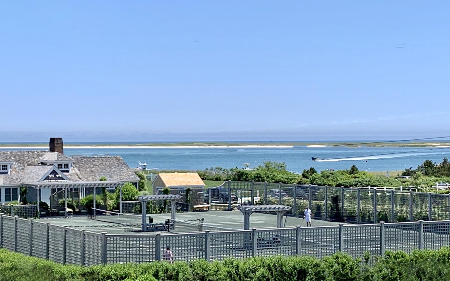 Coastal house with tennis court and ocean view under a clear blue sky.