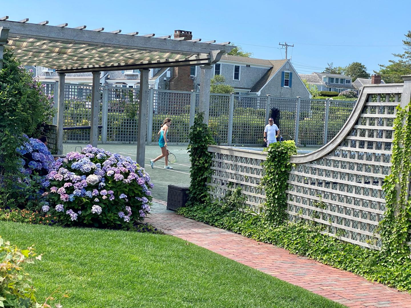 Lush garden with flowers near a tennis court under a clear blue sky.