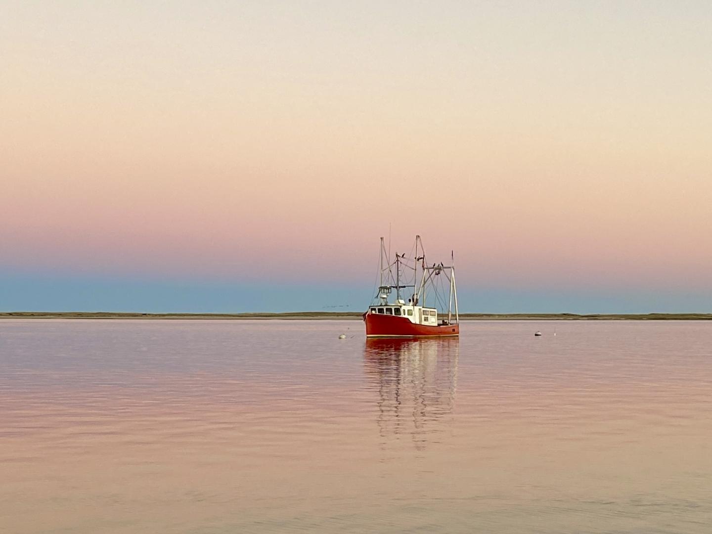 Red boat on calm water with a pastel sunset sky.