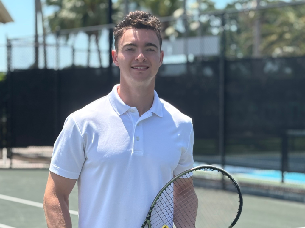 Man in a white shirt holding a tennis racket on an outdoor court.