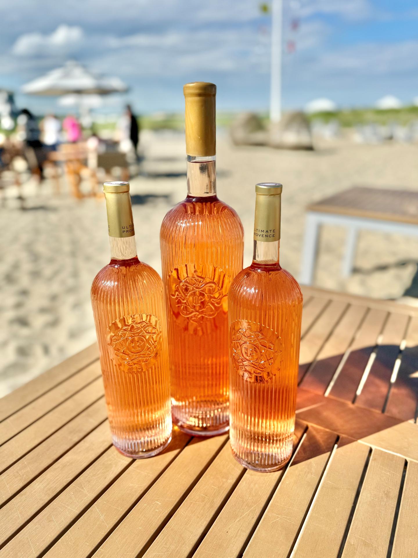 Three bottles of rosé wine on a wooden table at the beach.