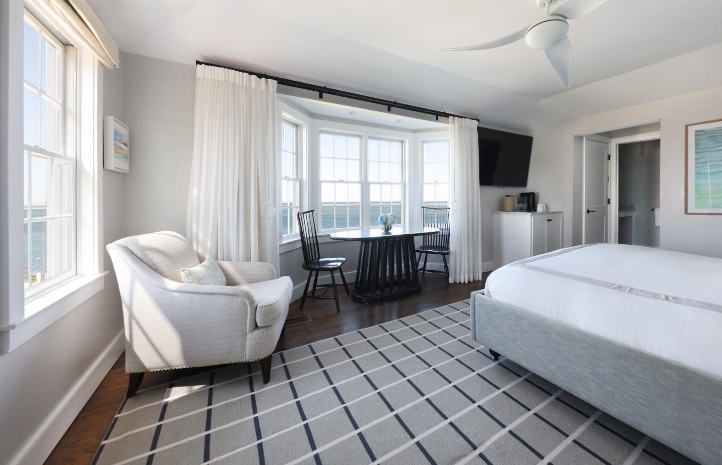 Bright bedroom with large windows, white decor, and a patterned rug.