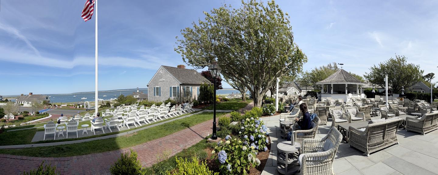 Coastal garden with chairs, gazebo, trees, and American flag under clear blue sky.