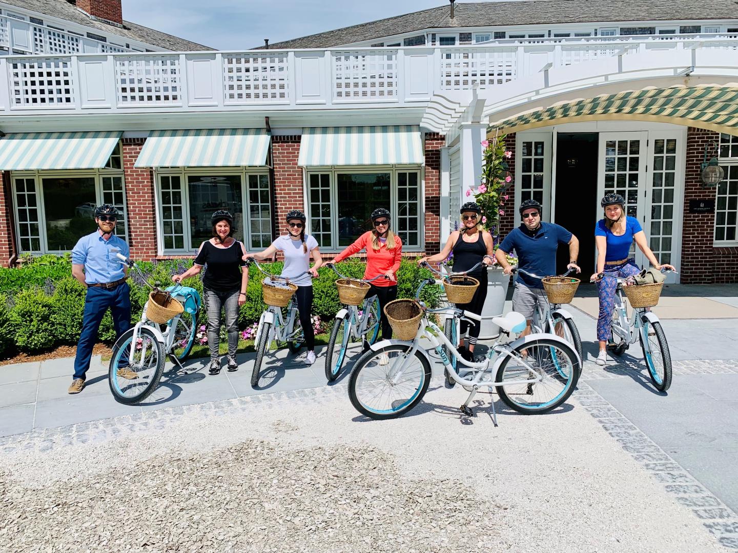 Group of people with bicycles in front of a large building with striped awnings.