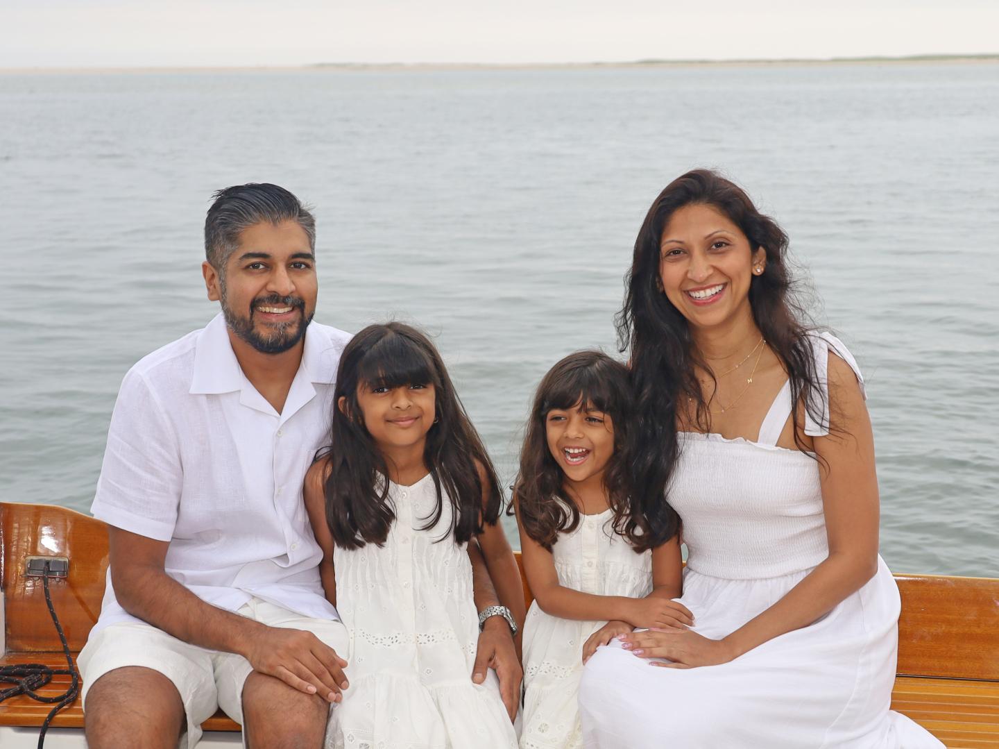 Family in white sitting on a boat with a calm sea in the background.