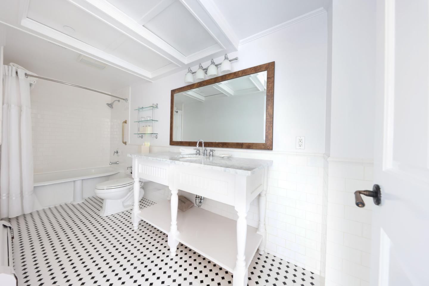 White bathroom with black and white tile floor, large mirror, and a double sink.