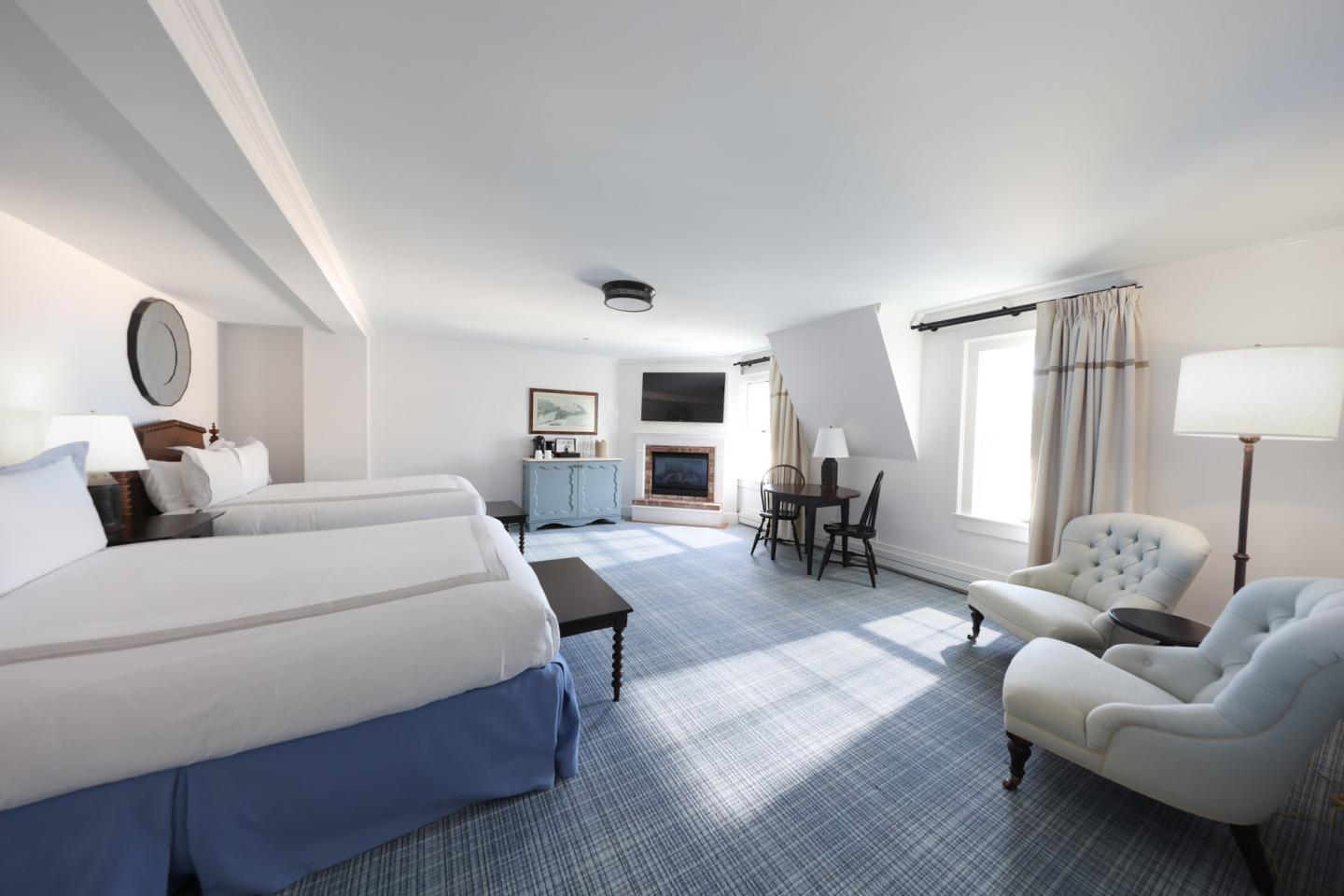 Bright hotel room with two beds, blue chairs, and a large window.