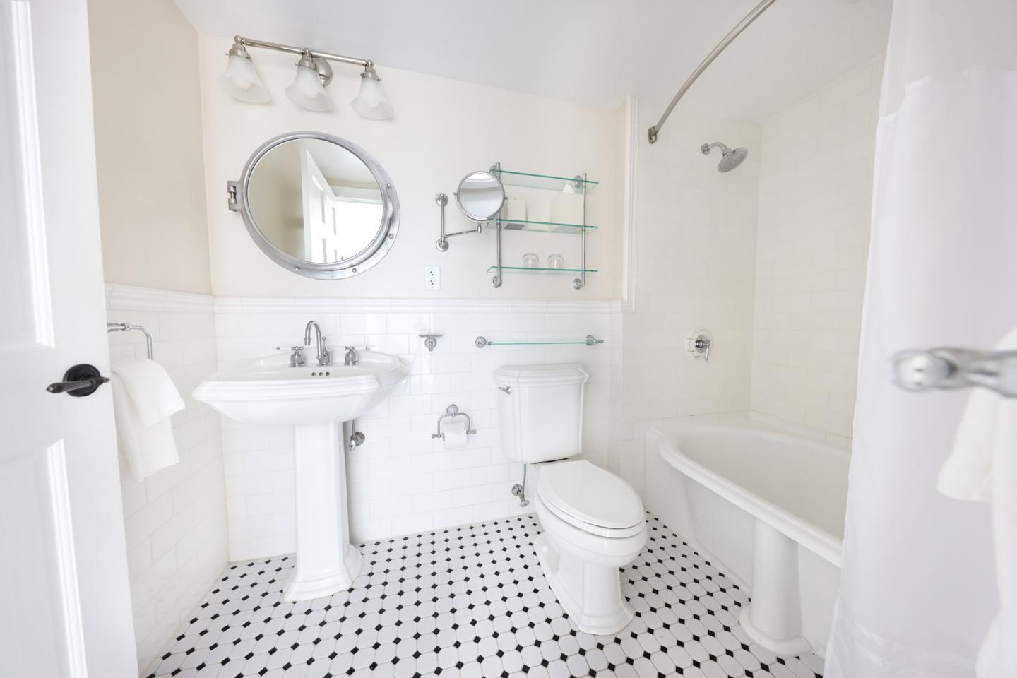 Bright white bathroom with pedestal sink, toilet, and bathtub. Circular mirror above sink.