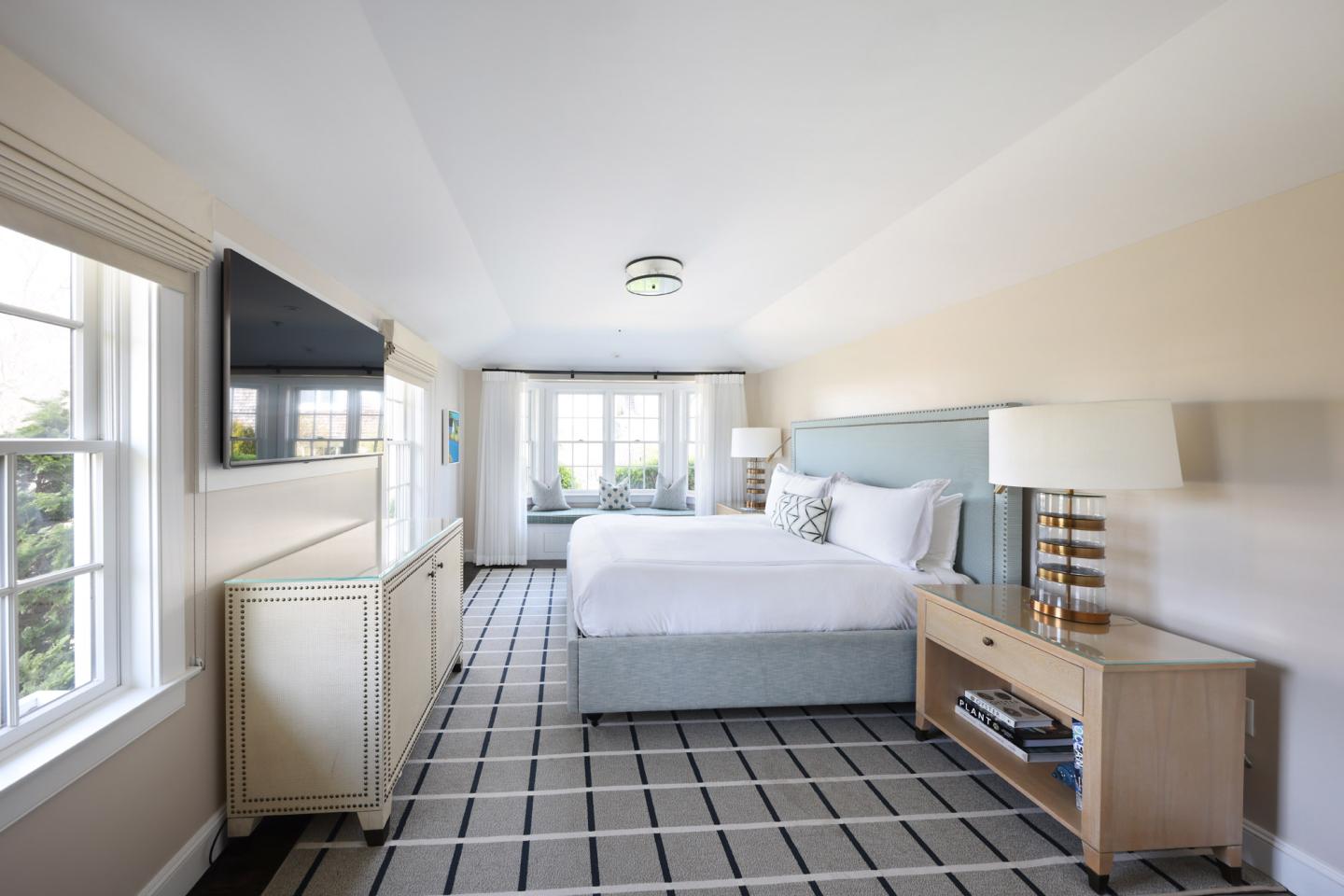 Bright bedroom with a large bed, modern decor, plaid carpet, and large windows.