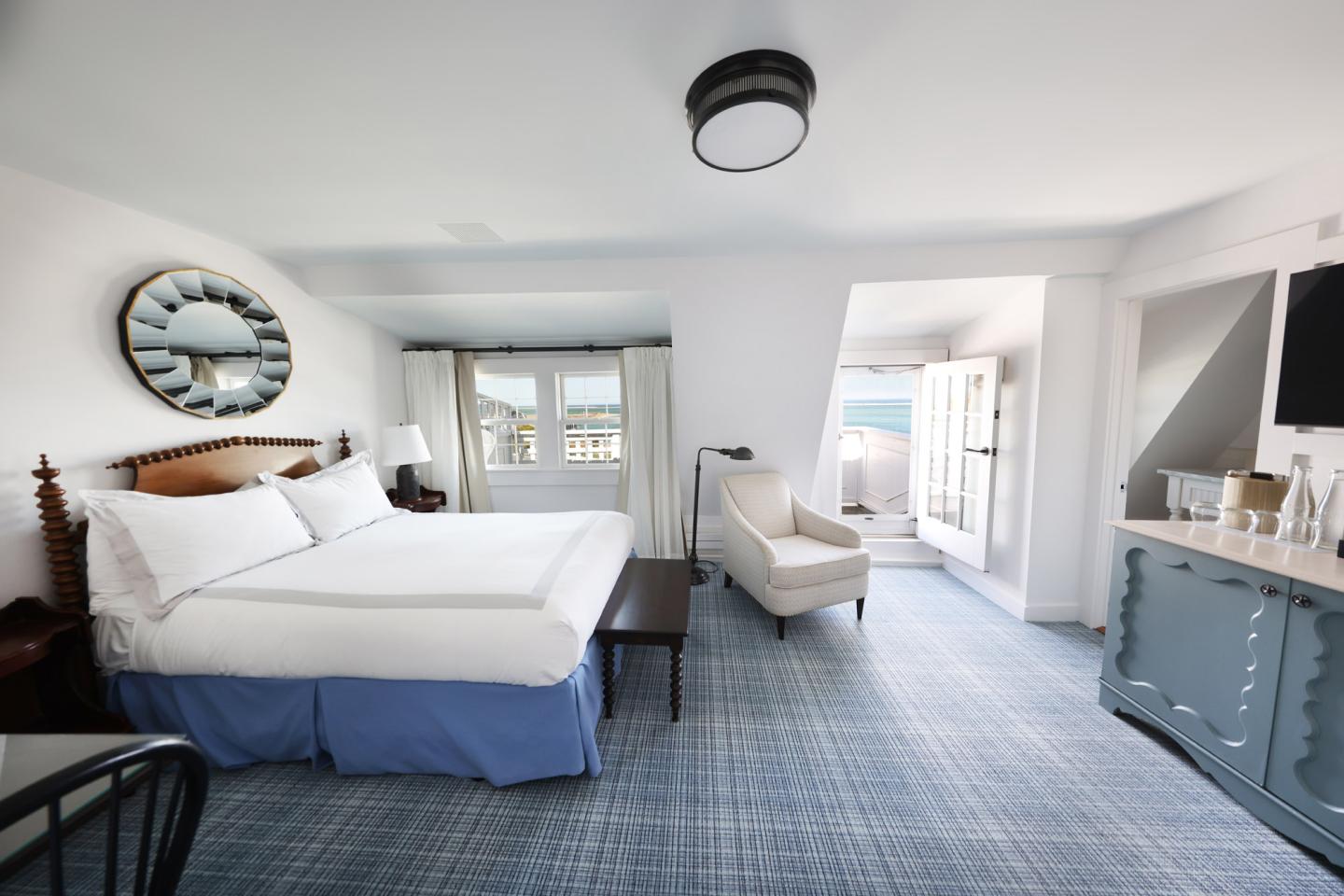 Spacious hotel room with a large bed, armchair, and ocean view balcony.