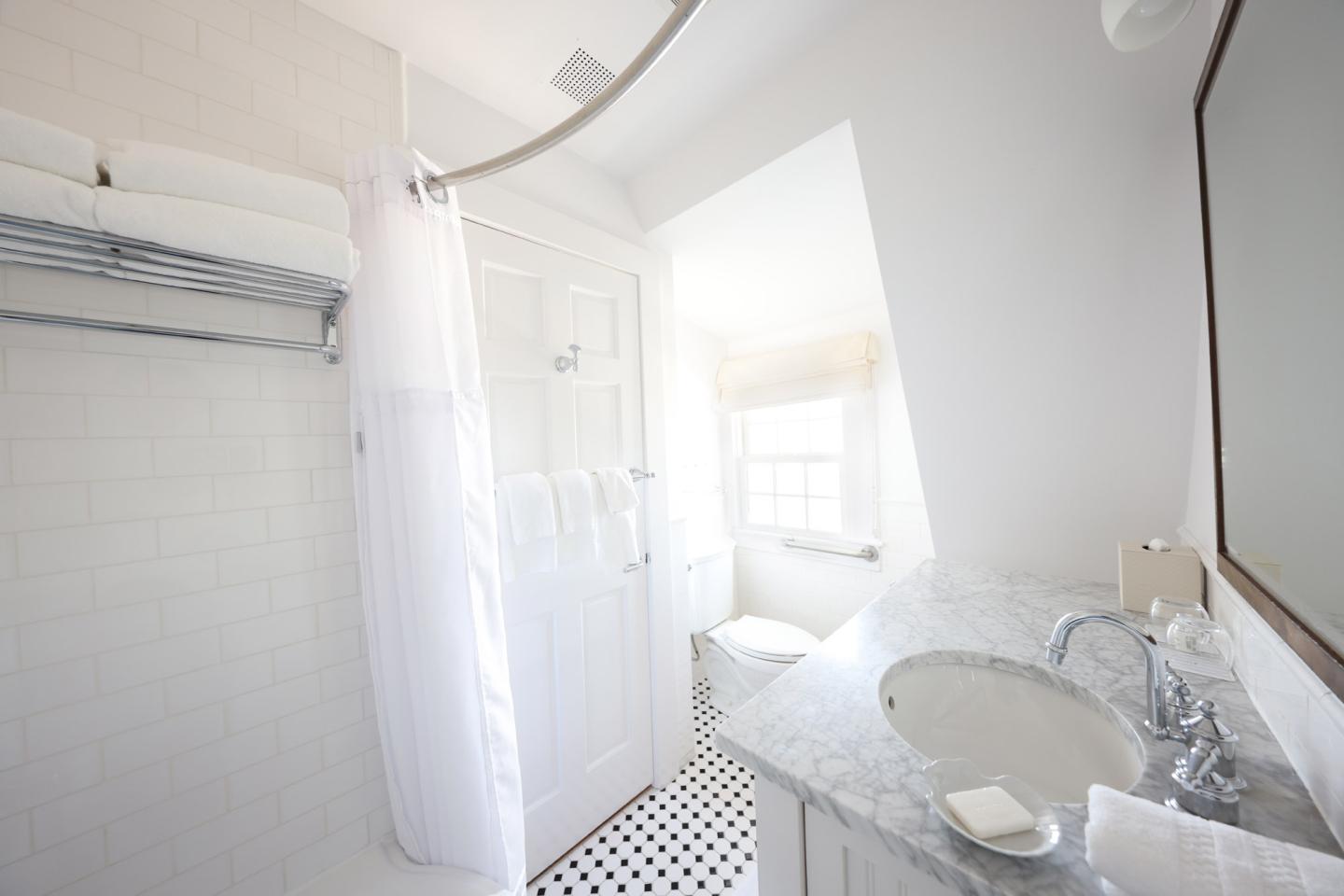 Bright white bathroom with shower, towels, and marble countertop.