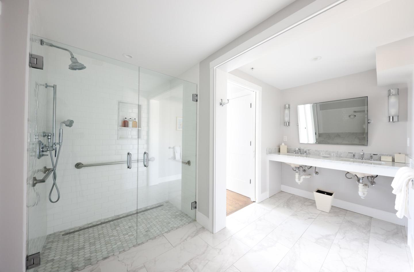 Modern white bathroom with glass shower and double sinks.
