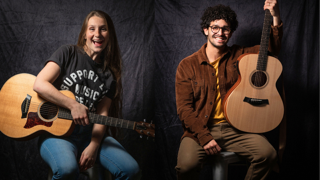 Two people with guitars smiling against a dark backdrop.