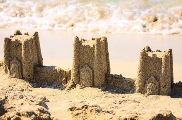 Sandcastle with three towers near ocean waves.