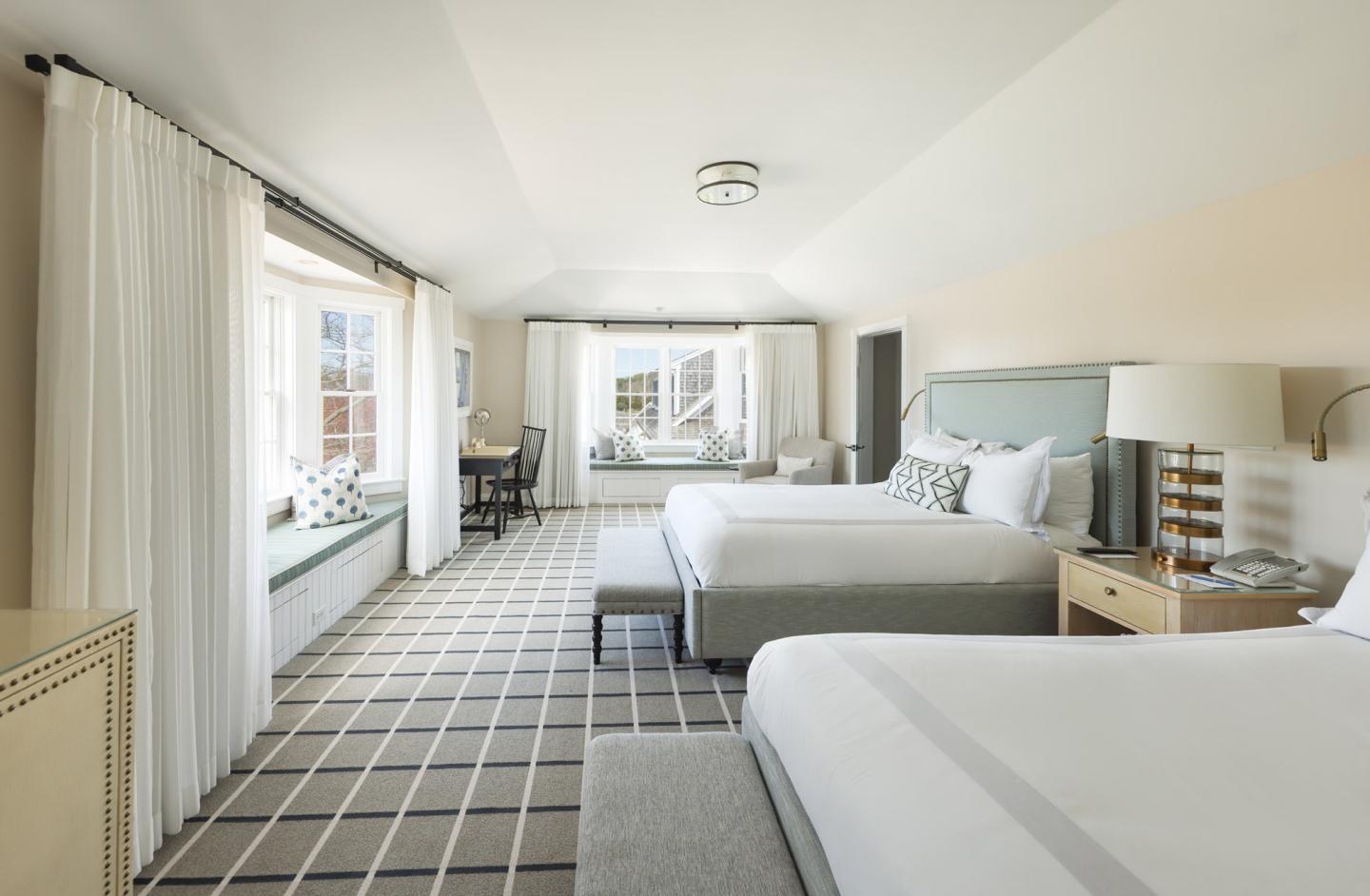 Bright hotel room with two beds, large windows, and a patterned carpet.