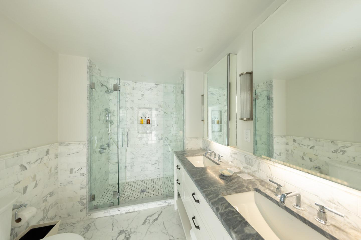 Luxurious bathroom with marble walls, large mirror, and glass shower.