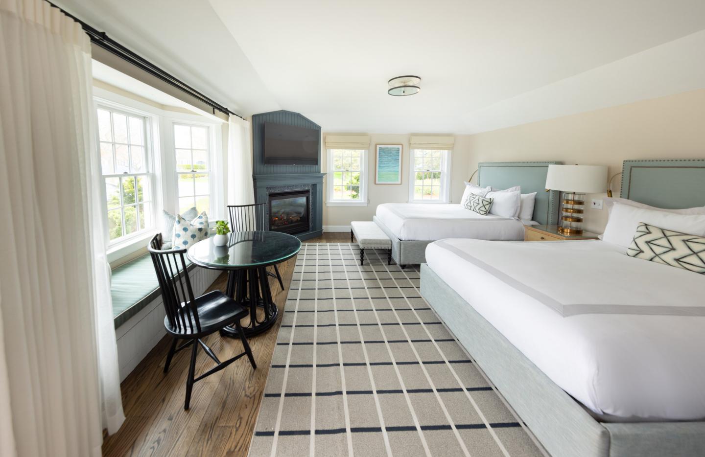 Bright hotel room with two beds, a fireplace, and a window-side seating area.