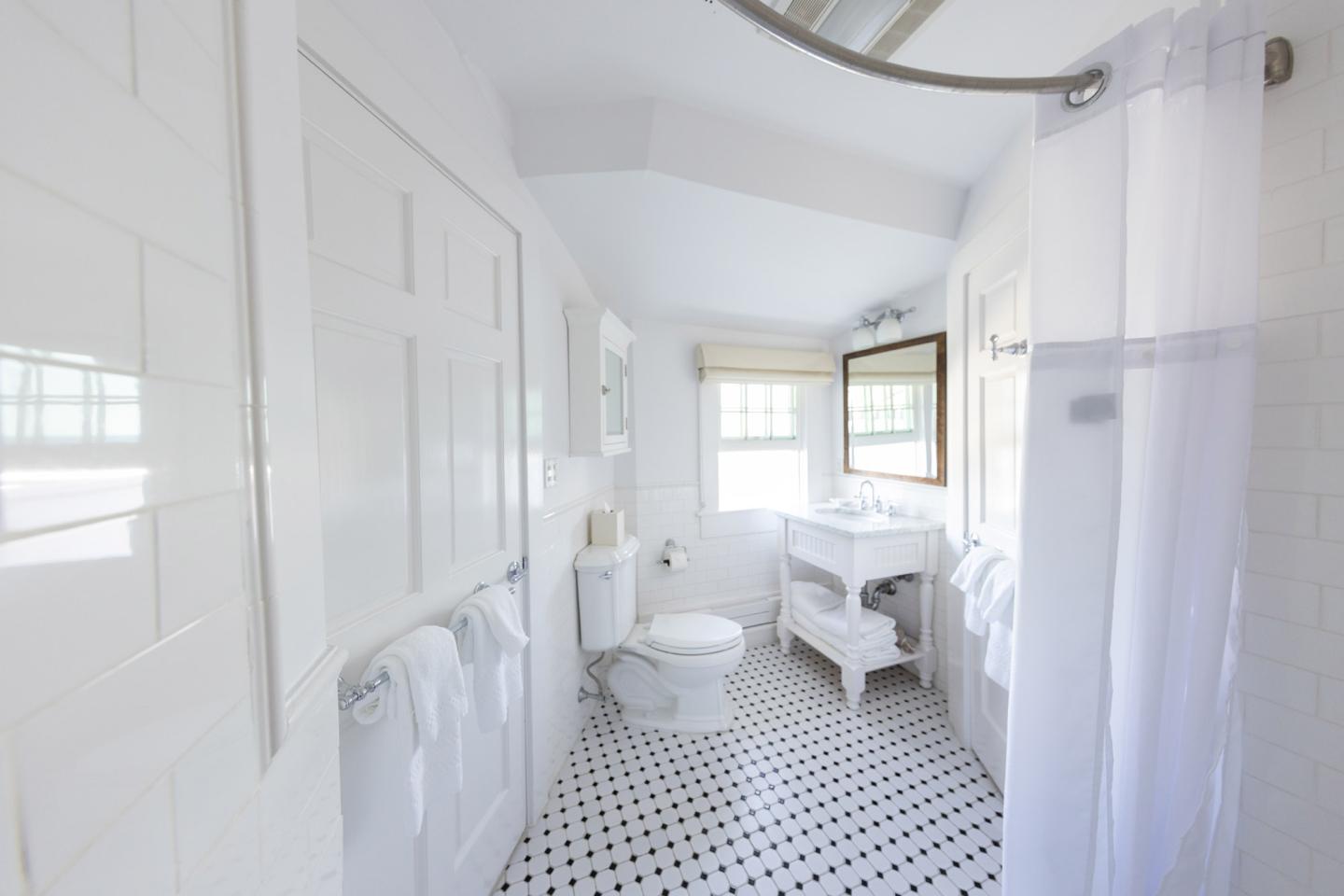 Bright white bathroom with tiled floor, shower, and window.