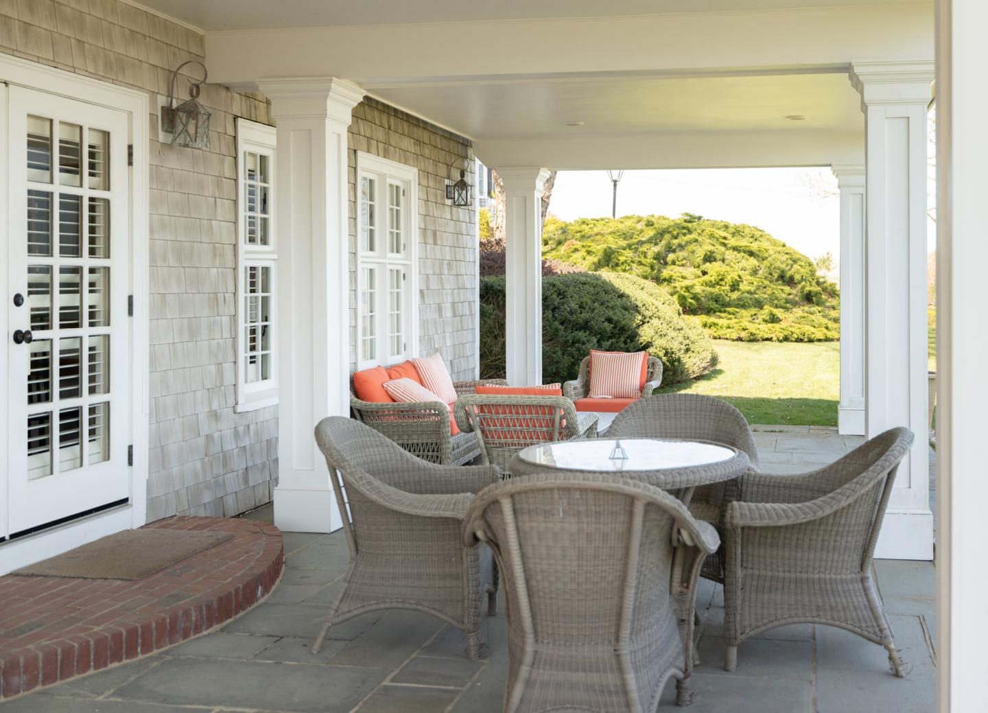 Covered patio with wicker chairs and table, view of garden and bushes.
