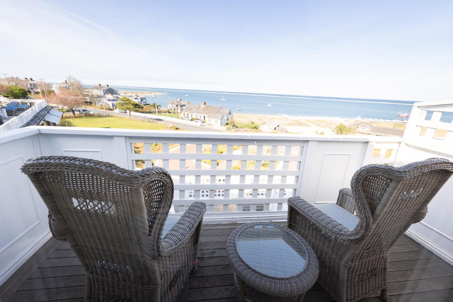 Two wicker chairs on a balcony overlook the ocean.
