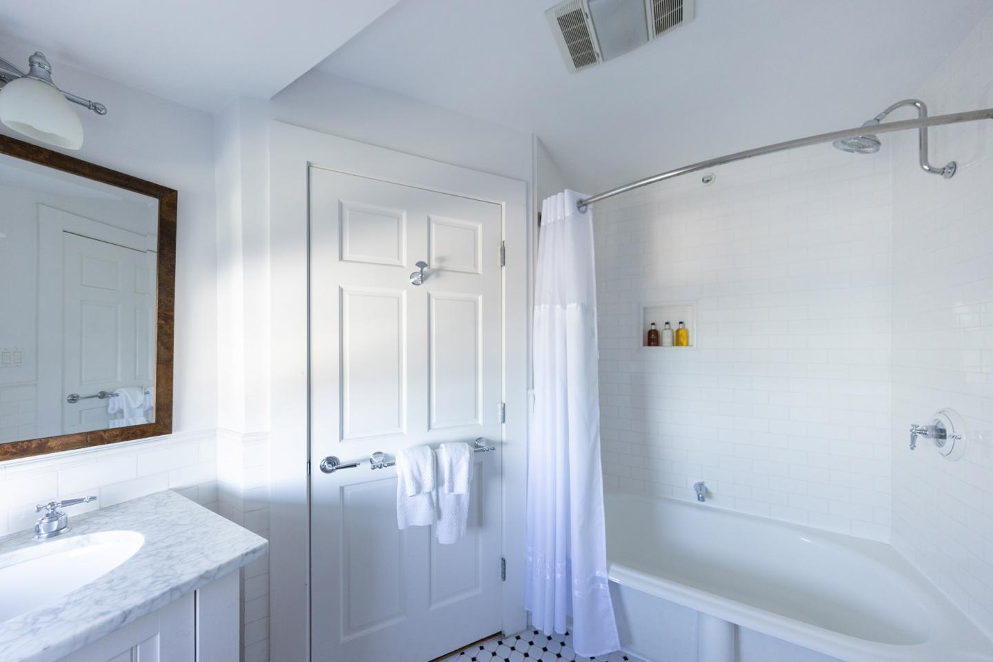 Bright white bathroom with a bathtub, sink, mirror, and door.