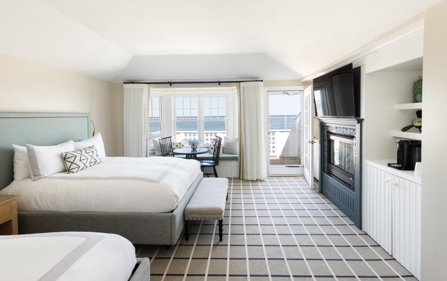 Bright hotel room with two beds, fireplace, and balcony view.