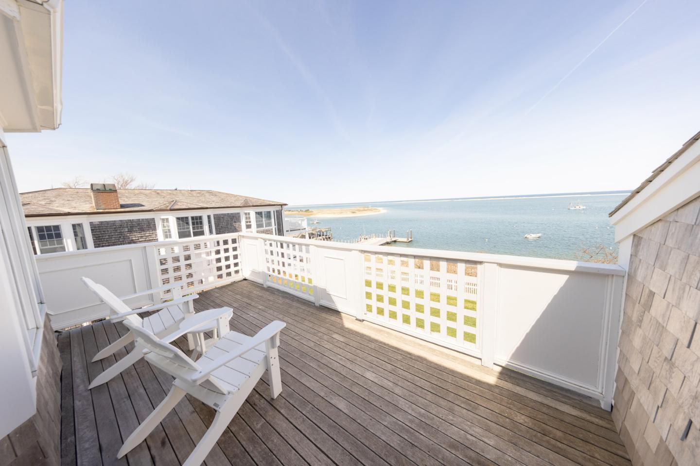 Sunny seaside deck with two white chairs overlooking the ocean.