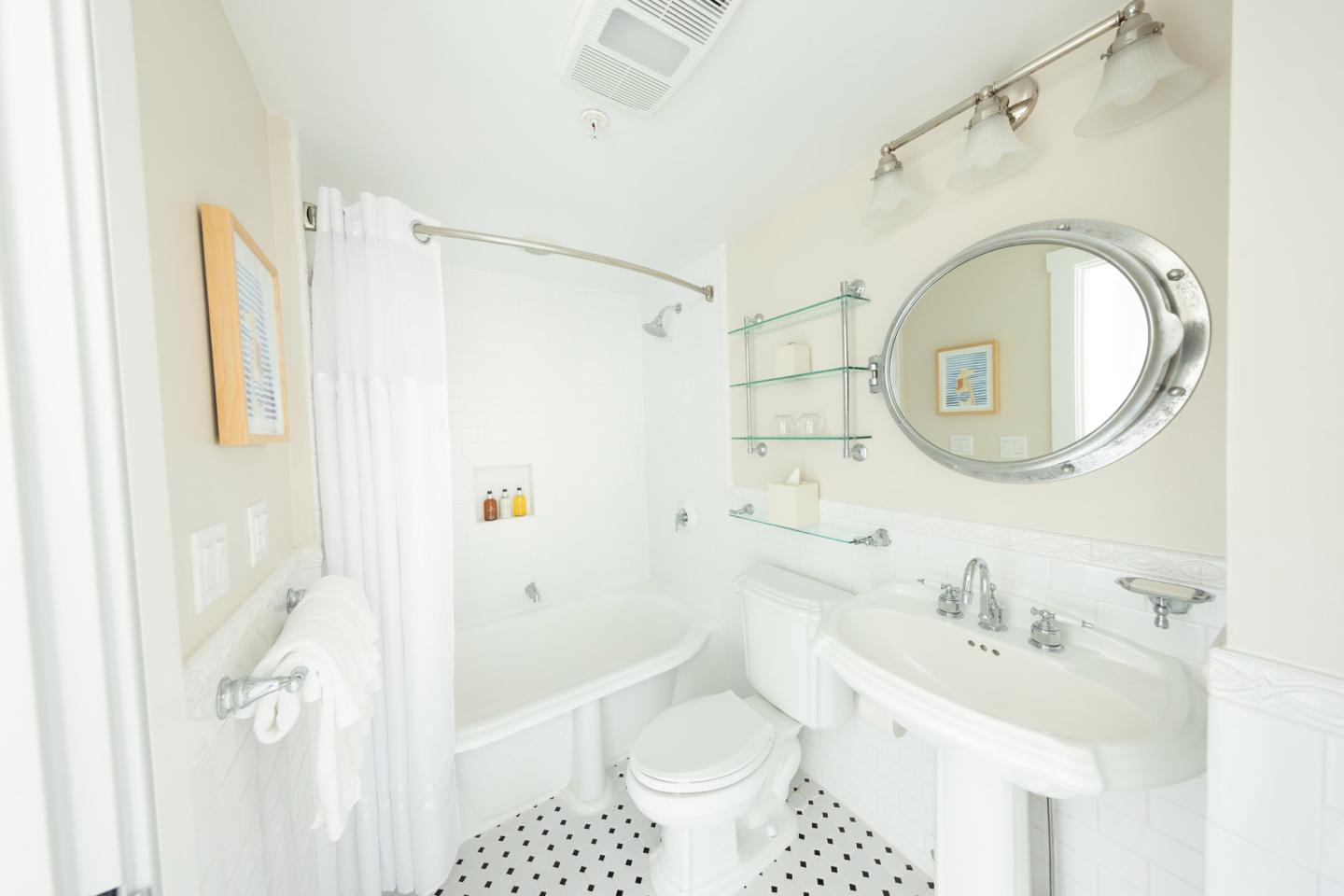 Bright white bathroom with tub, sink, toilet, and oval mirror.