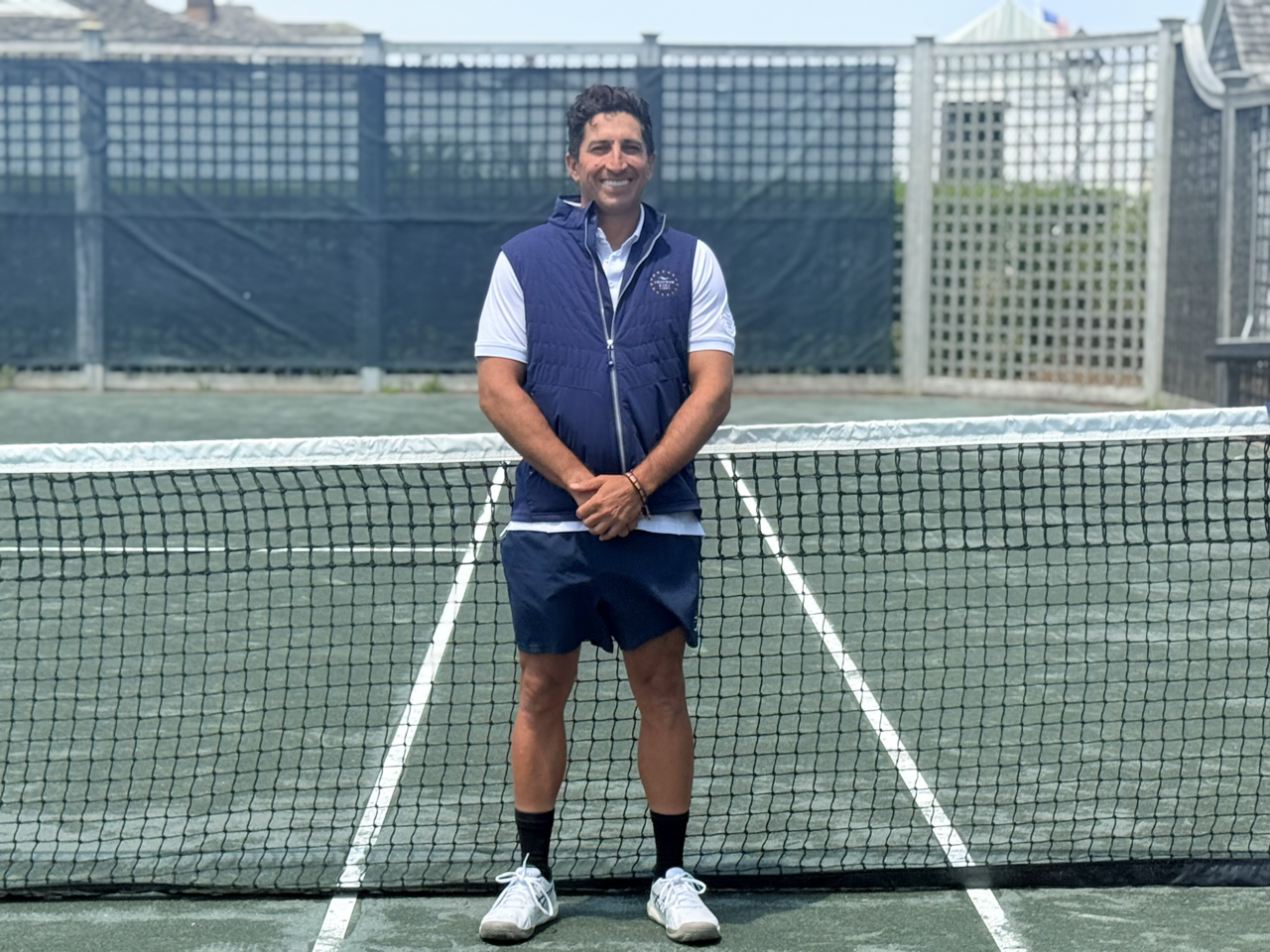 Man standing on a tennis court, smiling, with a net behind him.