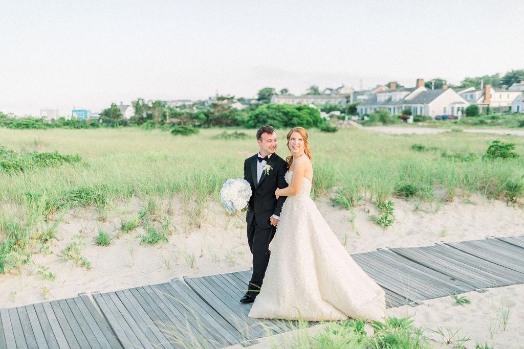 Bride and groom smiling on a boardwalk near a grassy field.