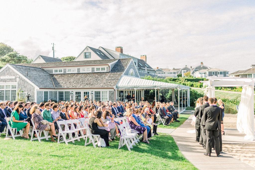 Wedding ceremony outdoors with guests seated and bridal party standing at the altar.