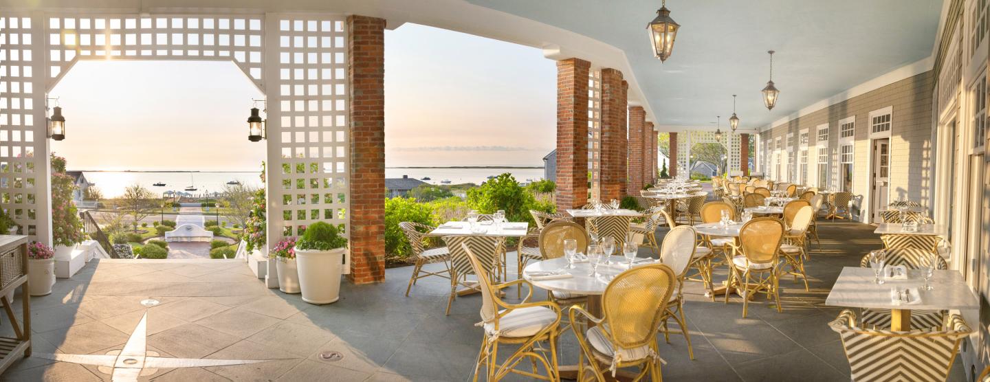 Elegant outdoor patio with white wicker chairs and tables, overlooking ocean at sunset.