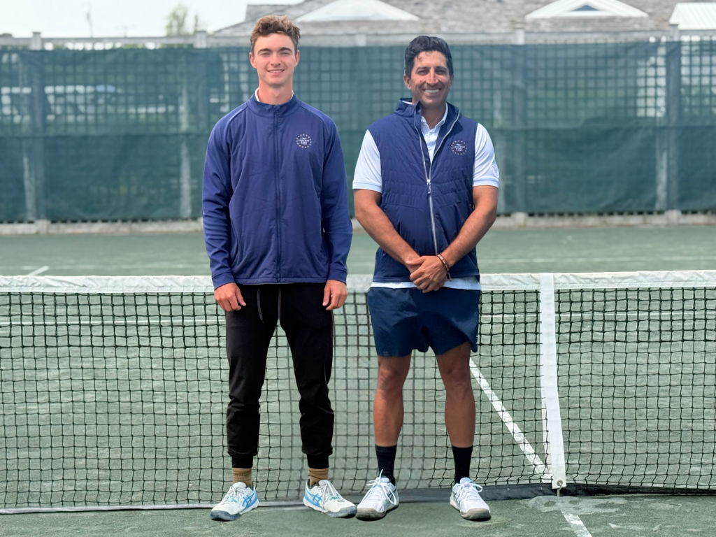 Two men smiling on a tennis court, standing in front of a net.