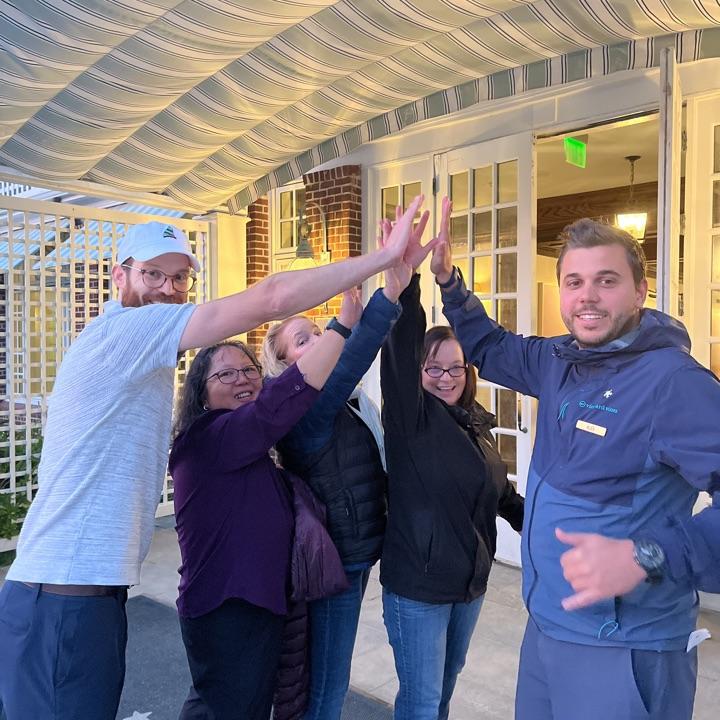 Group of people high-fiving outdoors, smiling warmly.